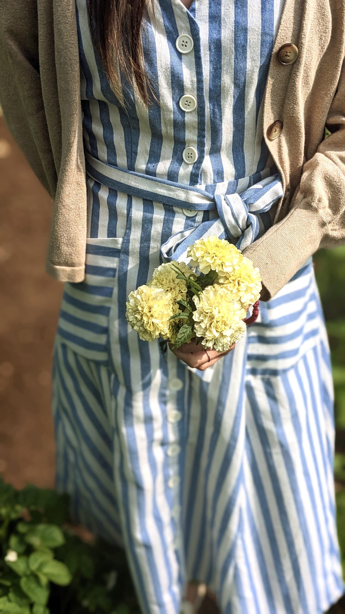 girl holding yellow marigolds in a blue striped dress and tan cardigan