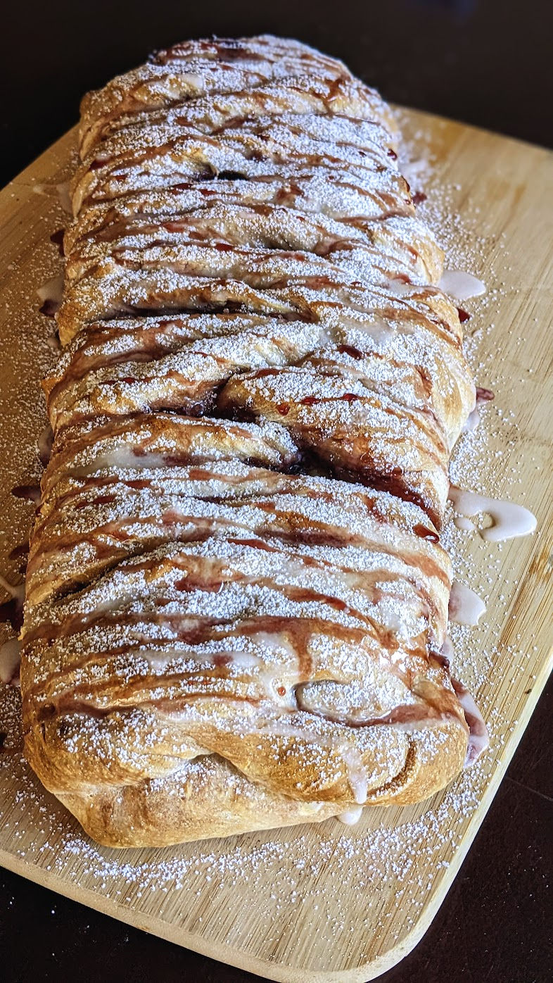 sourdough braided bread with cherry glaze and powdered sugar glaze on wooden cutting board