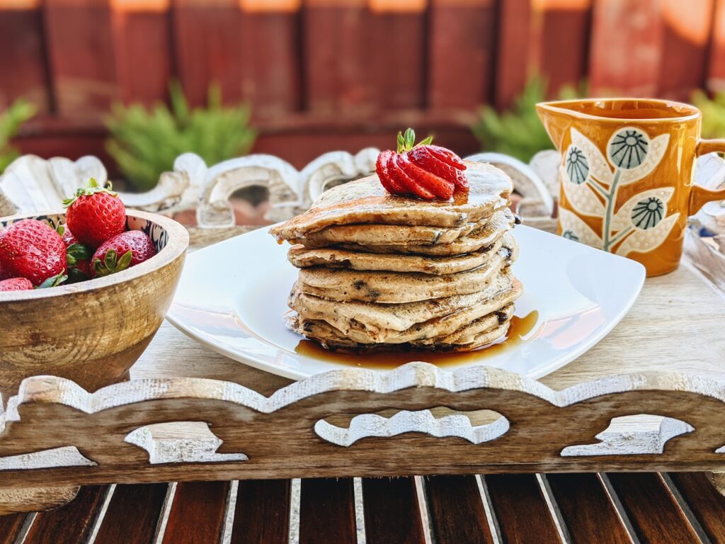 stack of pancake with bowl of strawberries and jar with maple syrup on a tray