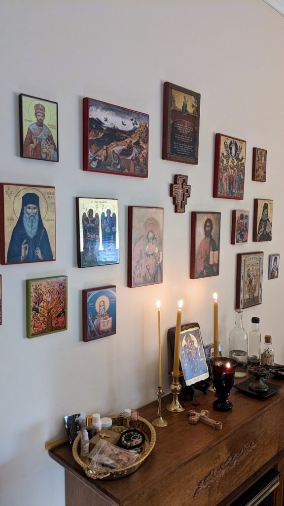 picture of icons hanging on the wall with candles below it sitting on a mantle