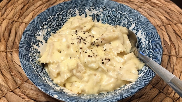 bowl of cheesy macaroni and cheese with a spoon on a rattan charger plate