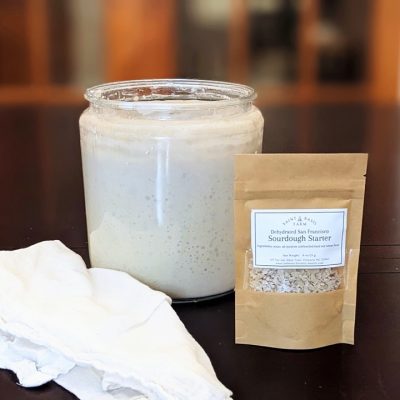 wide angle photos of dehydrated sourdough starter package in front of a bubbly sourdough starter jar