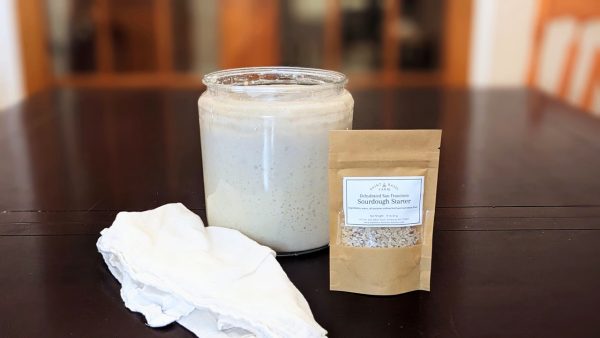 wide angle photos of dehydrated sourdough starter package in front of a bubbly sourdough starter jar